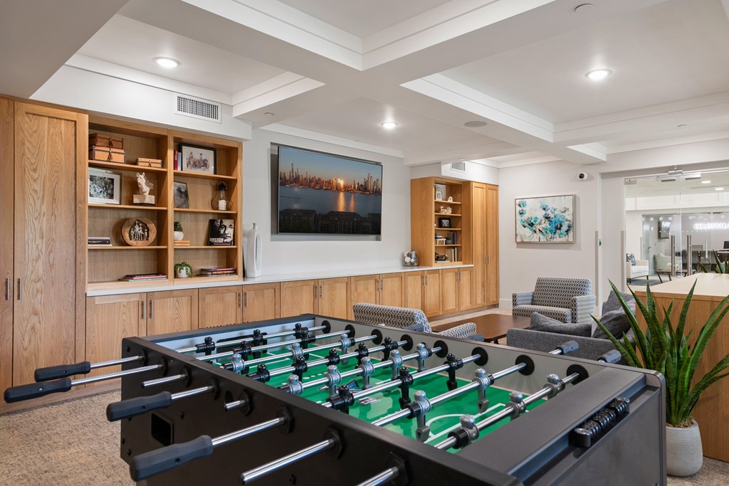 A foosball table is in the middle of a room with a TV and a cabinet with shelves.