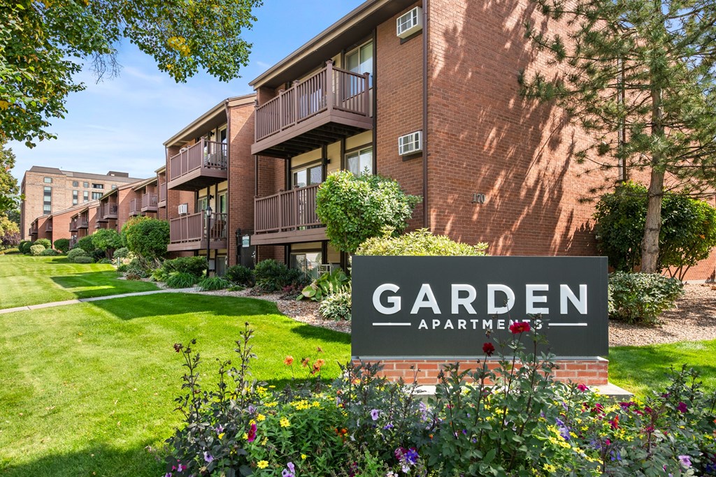 A sign that says Garden Apartments stands in front of a brick building.