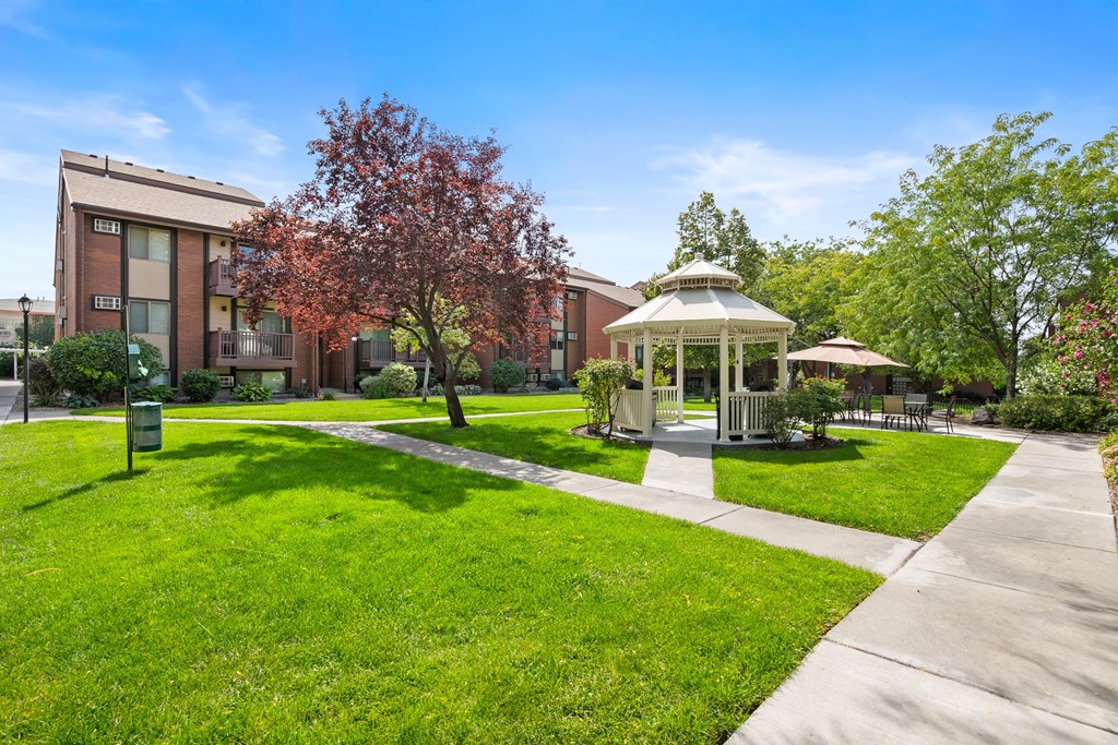 A gazebo is surrounded by a grassy area in front of a building.
