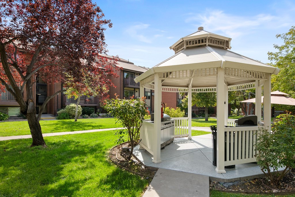 A gazebo is surrounded by a white fence and a tree with red leaves.