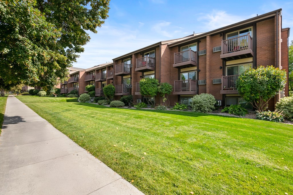 A row of brick apartment buildings with green lawns in front.