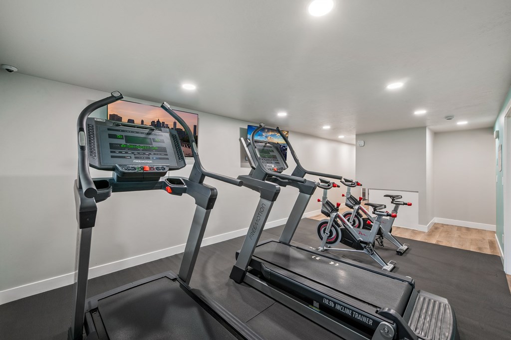 A treadmill with a screen and a handlebar is in a room with other treadmills.