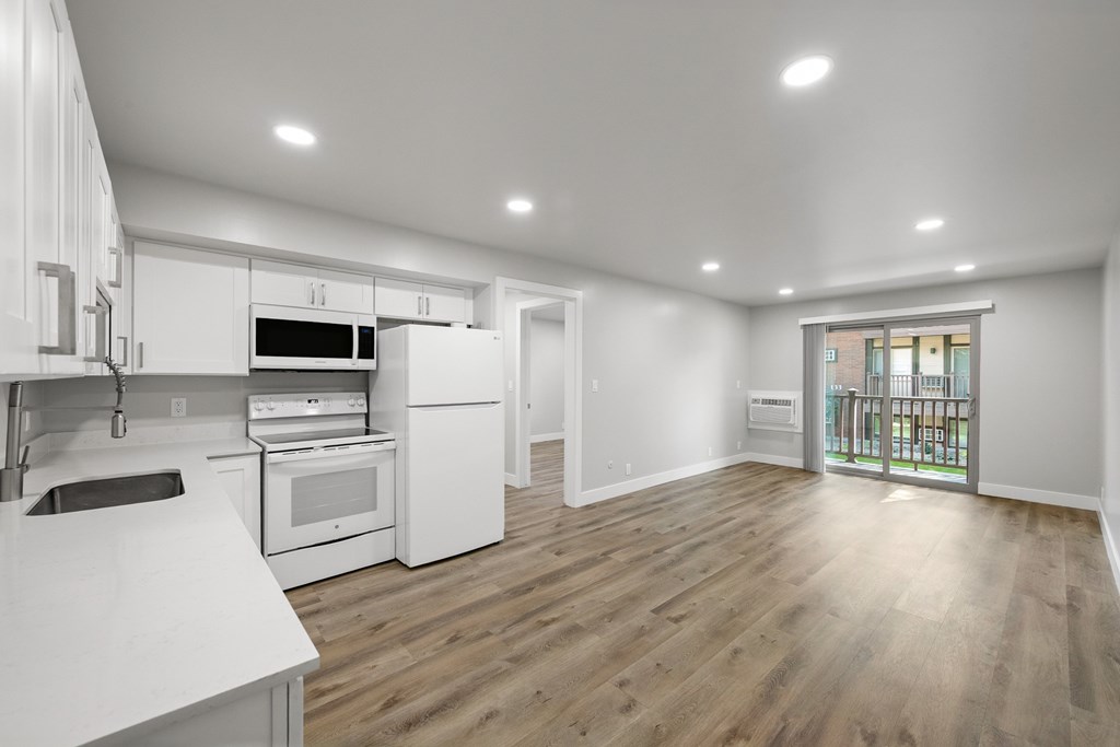 A spacious kitchen with white appliances and wooden flooring.