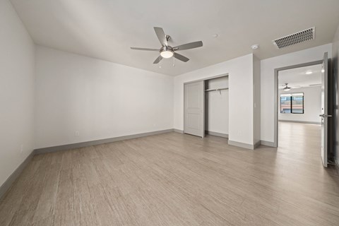 A room with a ceiling fan and light, hardwood floors, and a doorway leading to another room.
