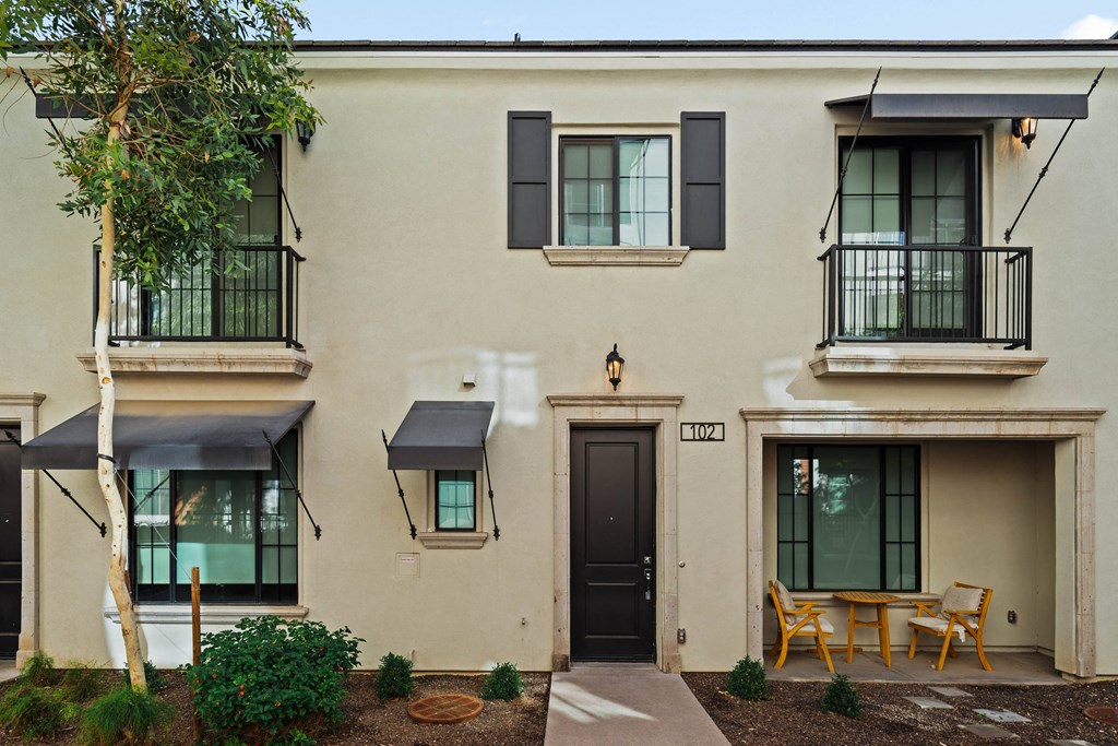 A beige building with black doors and windows has a small patio with a table and chairs.