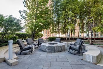 A stone fire pit sits in the middle of a patio surrounded by chairs.