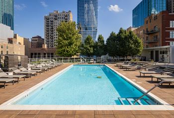 A large swimming pool with a blue tinted water surrounded by a wooden deck and lounge chairs.