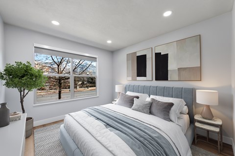 A bedroom with a large bed and a window overlooking a tree-lined street.