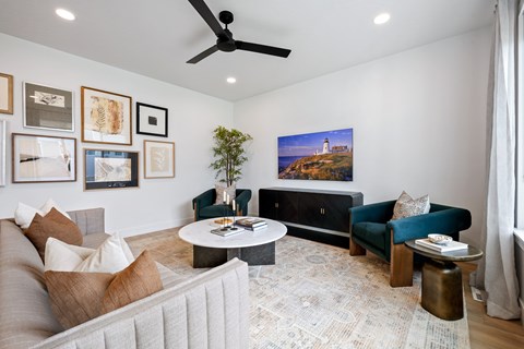 A living room with a grey couch, a green couch, a coffee table, and a painting of a lighthouse on the wall.