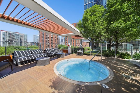 A hot tub on a wooden deck with a striped couch and trees in the background.