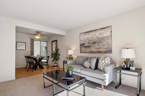 A living room with a grey couch, a glass coffee table, and a large abstract painting on the wall.