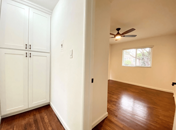 Bedroom Area with a Wide Window, Dark Hardwood Flooring, Spacious Cabinetry, and a Ceiling Fan at Jefferson Street Apartments in Santa Clara, CA, 95050