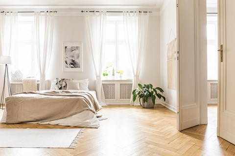 a bedroom with white curtains and a bed and a wood floor