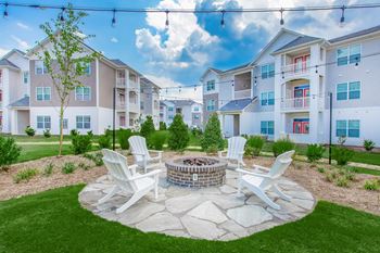 A fire pit surrounded by four chairs in a grassy area in front of apartment buildings.