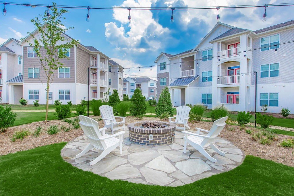 A fire pit surrounded by four chairs in a grassy area in front of apartment buildings.