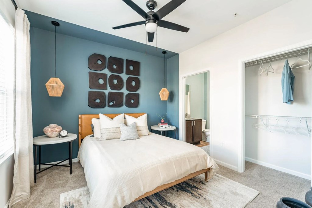 A bedroom with a bed, a ceiling fan, and a wall hanging.