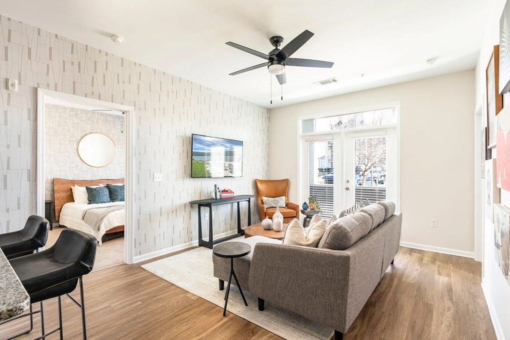 A living room with a grey couch, a black chair, and a white wall with a circular window.