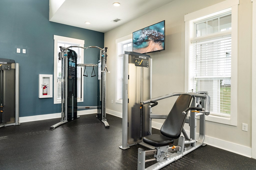 A home gym with a variety of equipment including a treadmill, a weight machine, and a television. at Concord Ridge Apartments, Concord, North Carolina