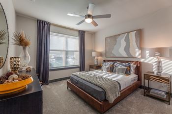 A bedroom with a bed, nightstand, and a ceiling fan. at Magnolia Grove Apartments, Terrell, Texas