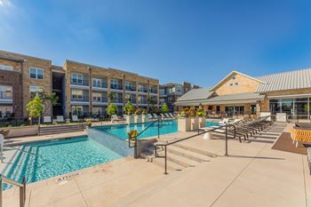 A swimming pool area with lounge chairs and a building in the background. at Magnolia Grove Apartments, Terrell, Texas