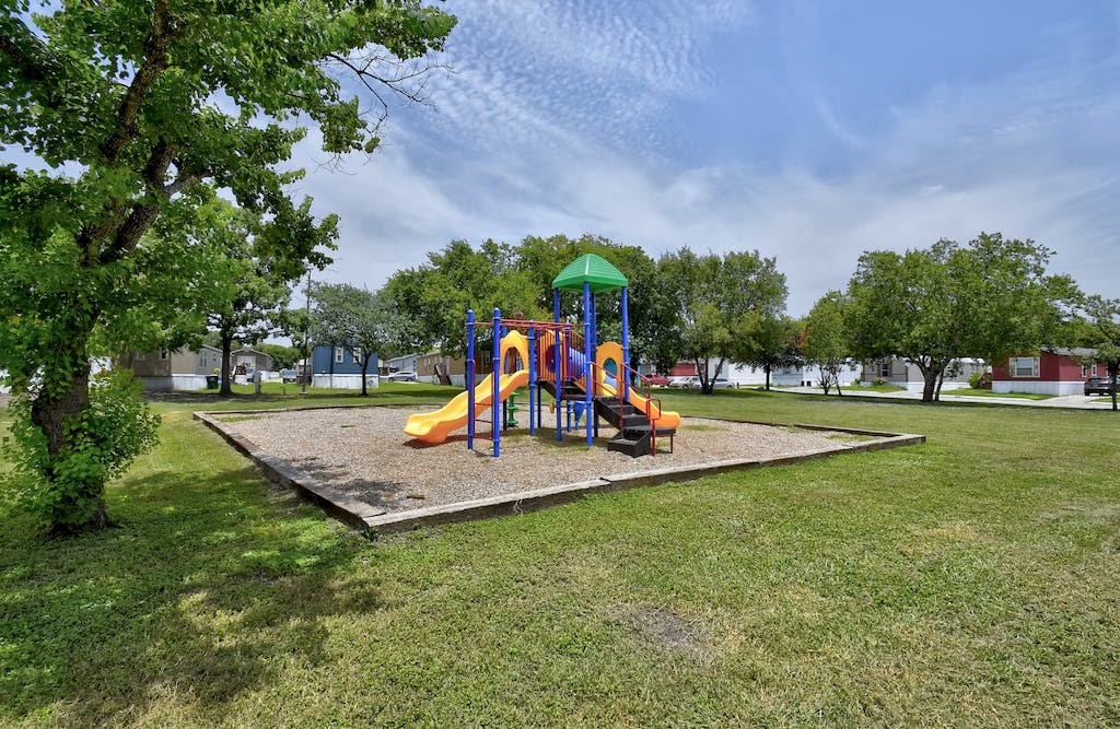 a playground with a swing set and sandbox in the middle of a grassy area with trees