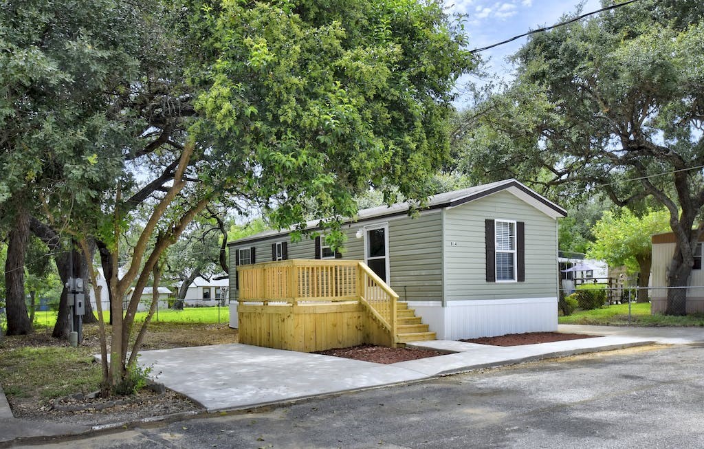 a mobile home with a porch and a deck with trees