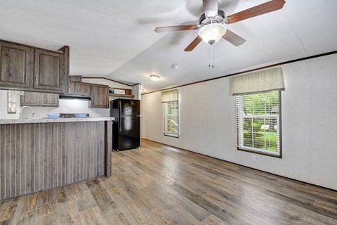 an empty living room with a kitchen and a ceiling fan