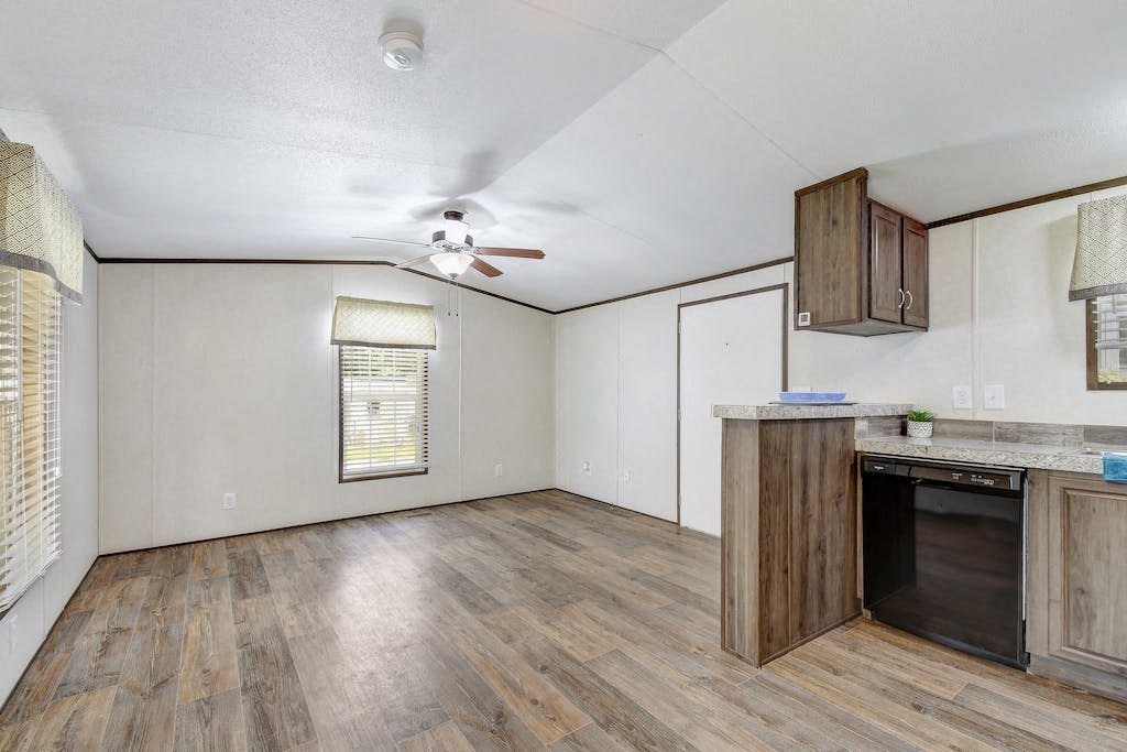 an empty living room with a kitchen and a ceiling fan