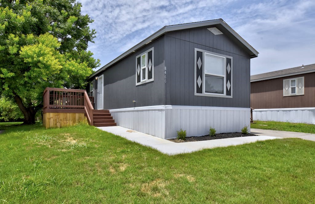 a gray house with white siding and a brown house in the background