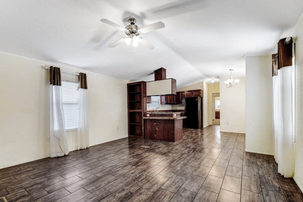 an empty living room with a ceiling fan and a kitchen