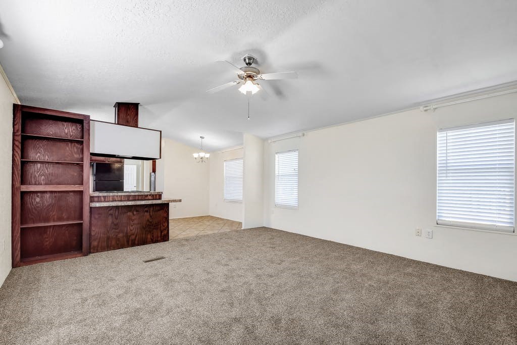 an empty living room with a ceiling fan and a bookshelf