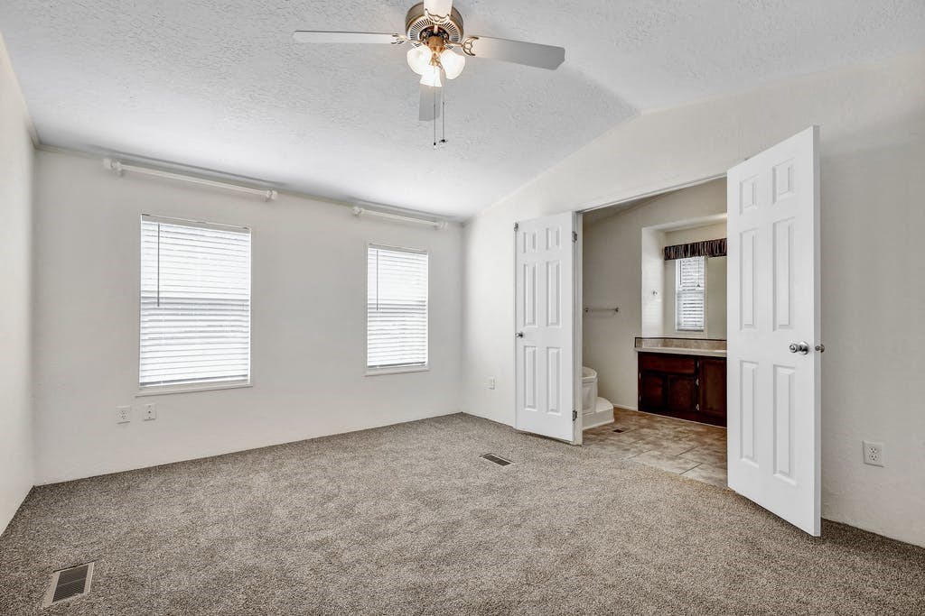 a bedroom with a ceiling fan and a bathroom in the background at Buckingham Village in Universal City, TX