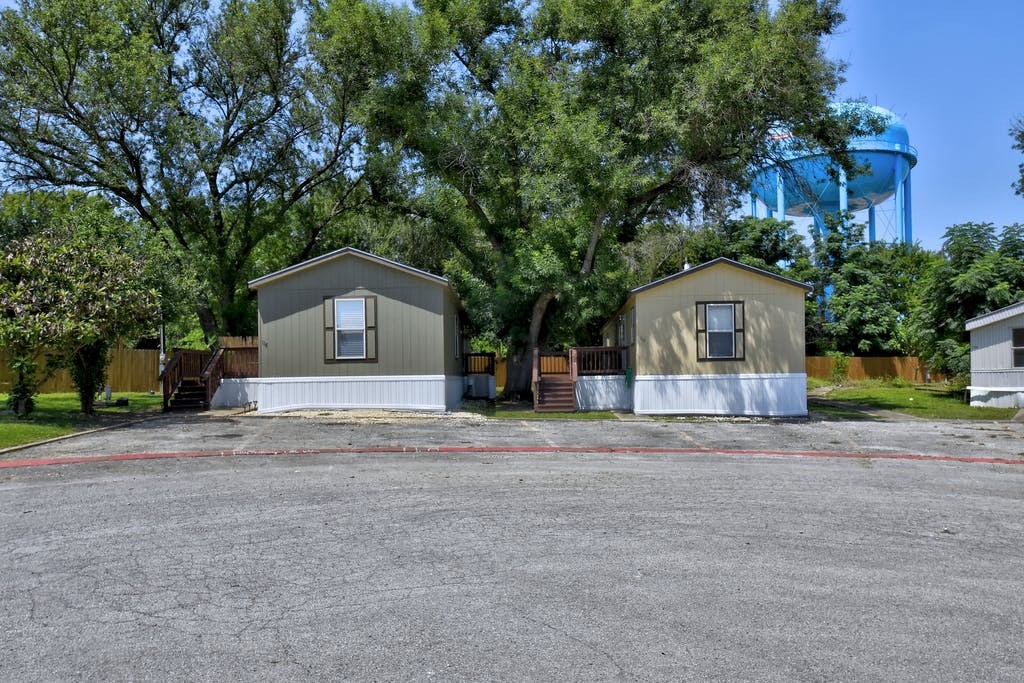 a parking lot in front of two sheds with trees and a water tower in the background