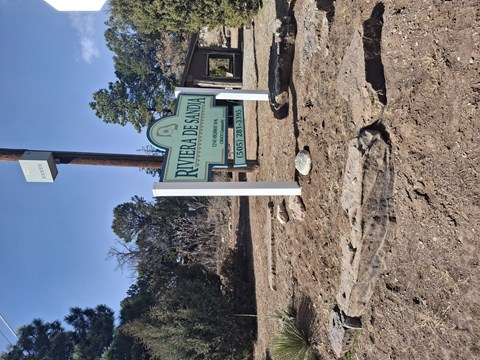 A sign for the Rivera de Arriba is mounted on a rocky wall.