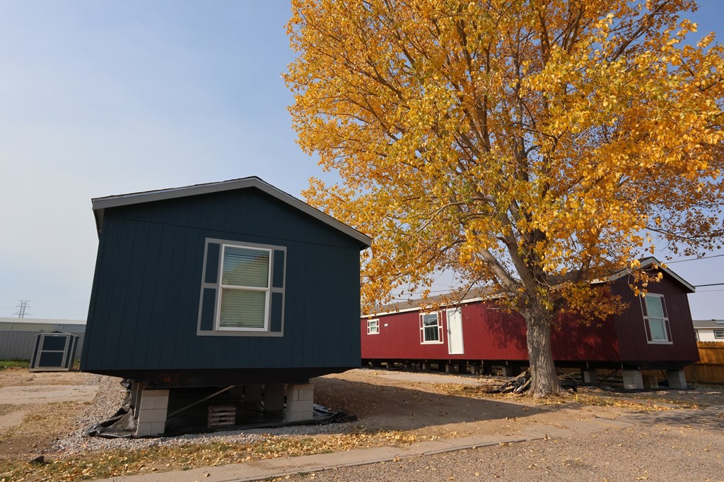 a black house with a red house behind it next to a tree at Country Lane, Cheyenne, WY