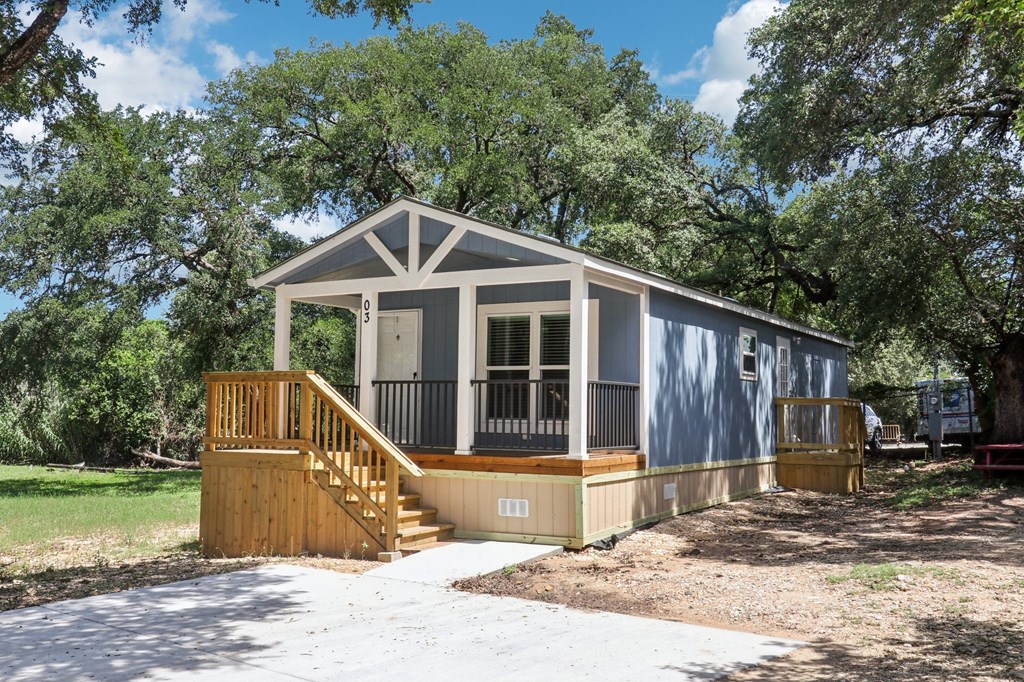 A small house with a porch and a deck is surrounded by trees.