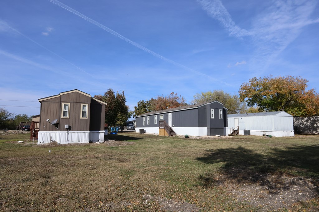 A small house with a grey roof is surrounded by a grassy field.