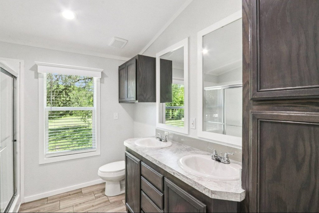 A bathroom with a toilet, double vanity sink, and mirror.
