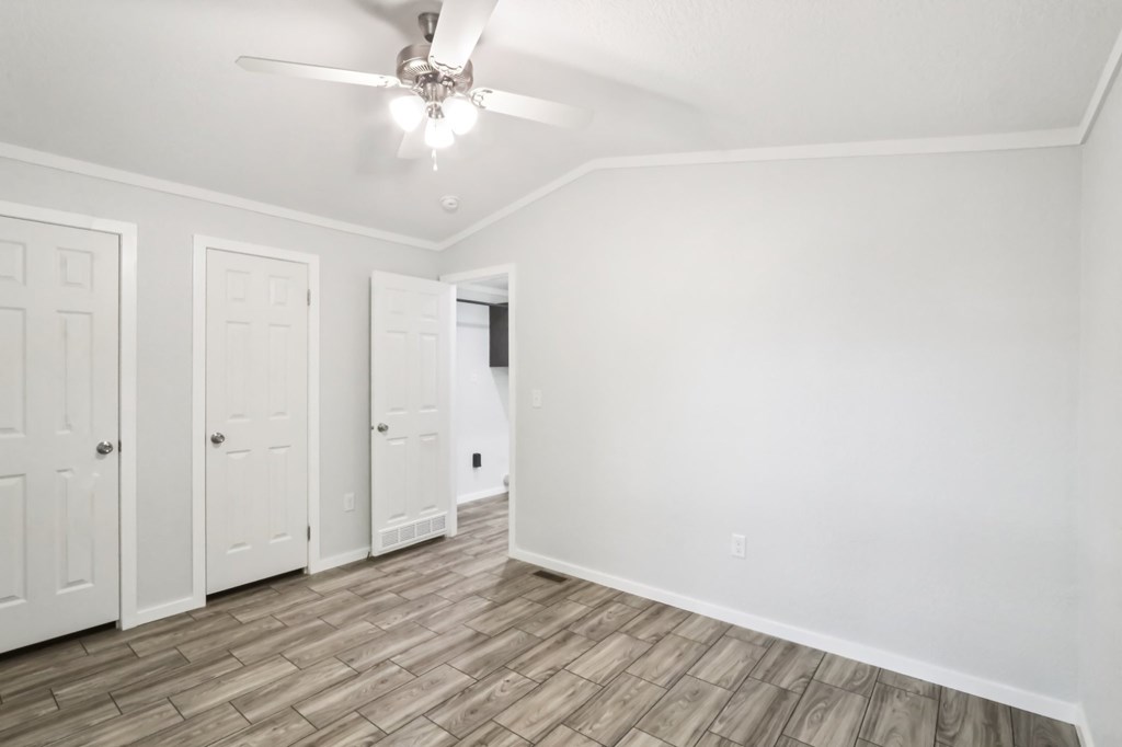 A room with a ceiling fan, large closet, and wood flooring.