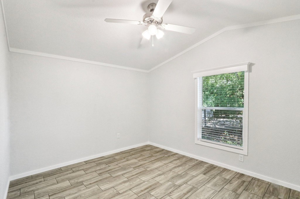 A room with a ceiling fan, faux wood blinds, and a window showing greenery outside.