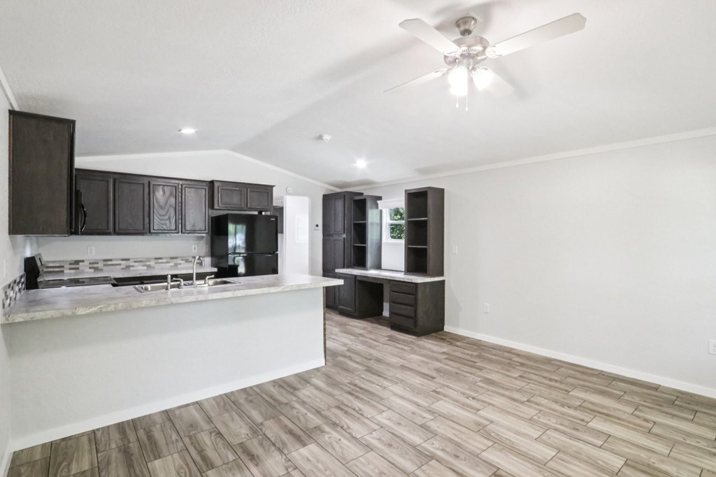 A spacious kitchen with dark brown cabinets and a white ceiling fan.