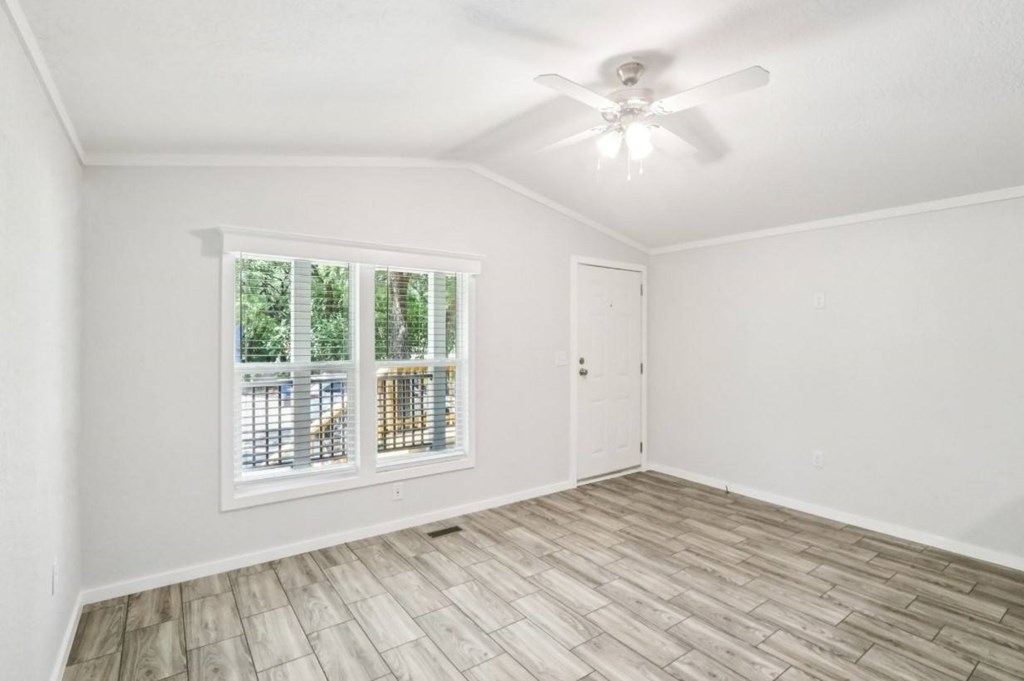 A room with a ceiling fan and a window with a view of trees and a fence.