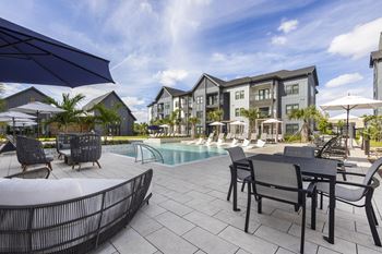 a swimming pool with tables and chairs and buildings in the background