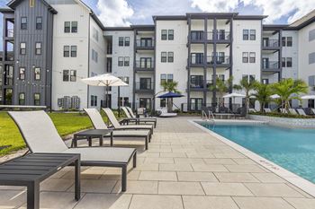 a swimming pool with chairs and umbrellas in front of an apartment building