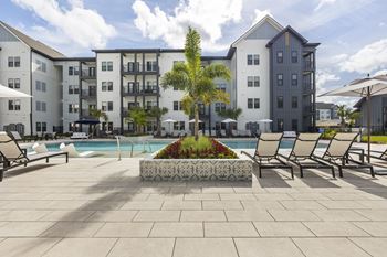 an outdoor pool with lounge chairs and a tree in front of an apartment building