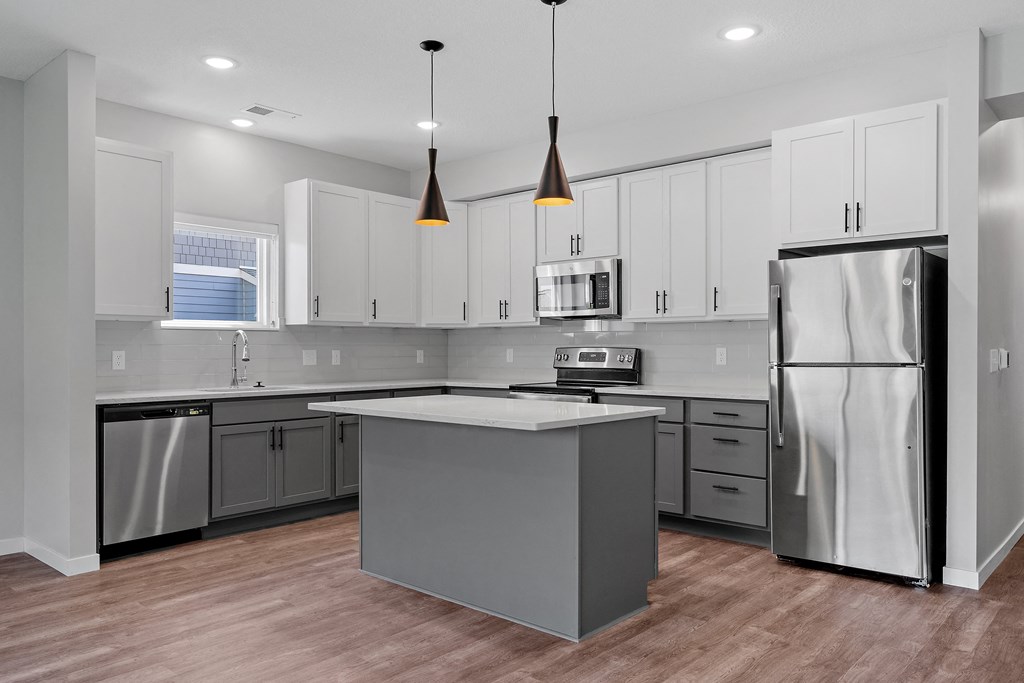 a kitchen with white cabinets and a gray island with a white countertop at The Lodge at Overland, Rochester, MN