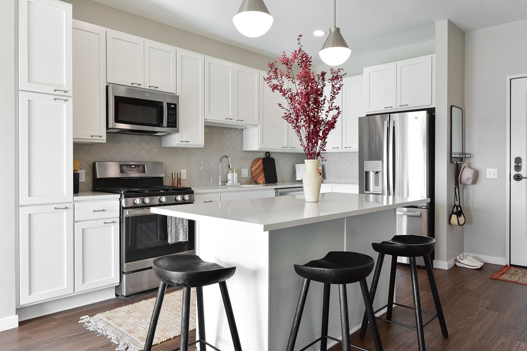 a kitchen with white cabinets and a white island with black stools at The Hallon Apartments, Hopkins, Minnesota