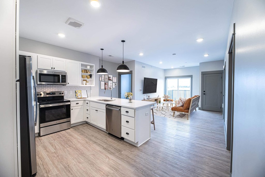 a kitchen and living room with white cabinets and stainless steel appliances at The Commons at Rivertown, Grandville, Michigan, 49418