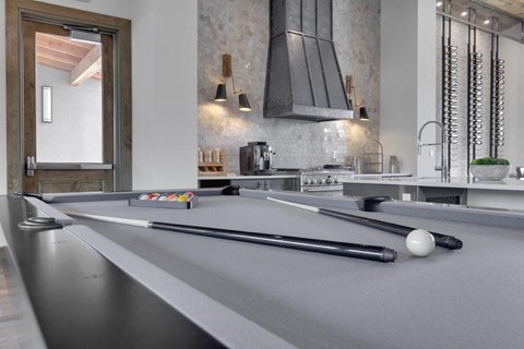 A pool table in a room with a kitchen in the background.