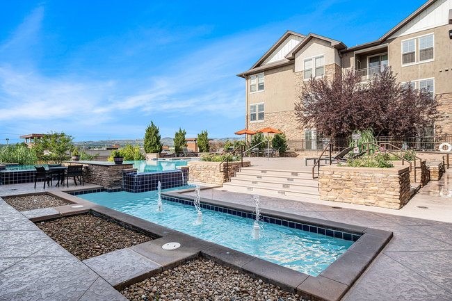 A large outdoor swimming pool with a waterfall and a patio area with chairs and a table.
